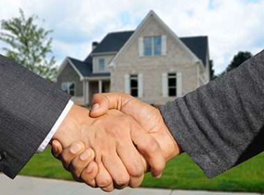 A house in the background and two people shaking hands